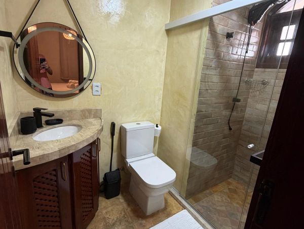 Cozy bathroom with marble sink, round mirror, toilet, and glass shower enclosure.