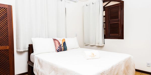Minimalist bedroom with white linens and a decorative pillow under soft lighting.