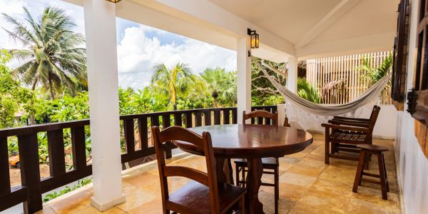 Cozy outdoor patio with wooden furniture and a hammock surrounded by tropical greenery.