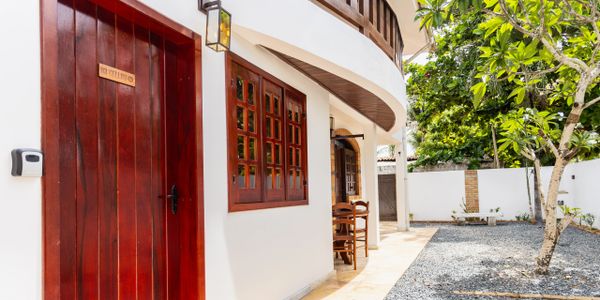 Cozy white house with wooden door and window, surrounded by a small garden and gravel path.