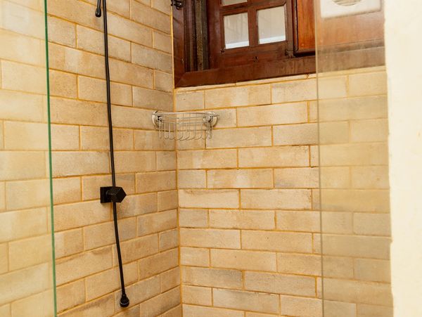 Minimalist shower area with beige tiles, a black showerhead, and a small window.