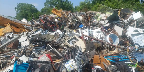 A large pile of assorted scrap metal and discarded household items outdoors.