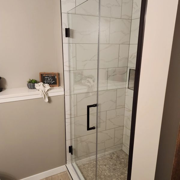 Modern glass shower with marble tile walls and pebble floor.