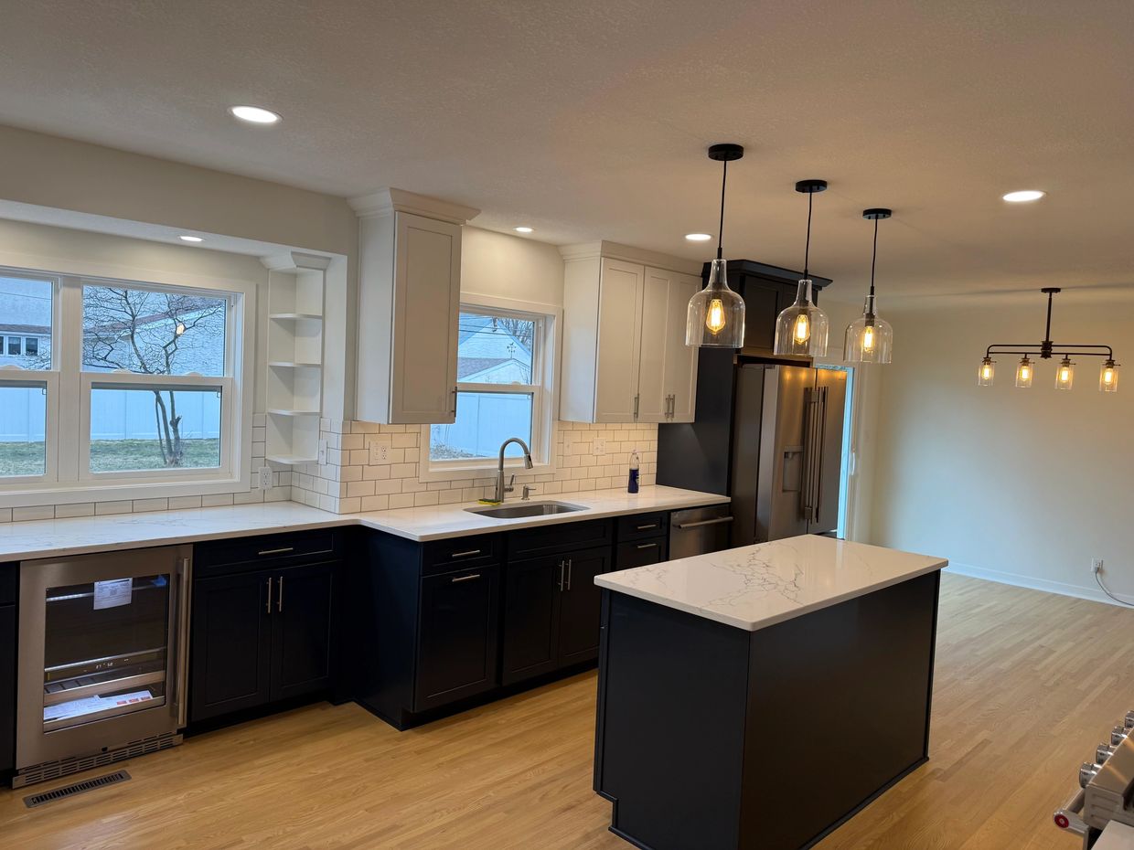 Modern kitchen with black and white cabinetry, marble countertops, and pendant lighting.