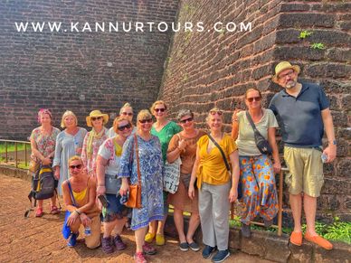 Group of tourists posing by an ancient stone wall under bright sunlight.