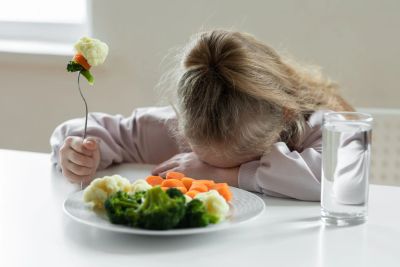 Child looks unhappy with her vegetables at the table.