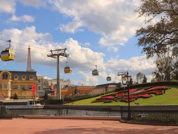 Cable cars crossing a park with a flower clock and Eiffel Tower replica.
