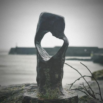 Abstract metal sculpture with a heart-shaped hole by the sea.