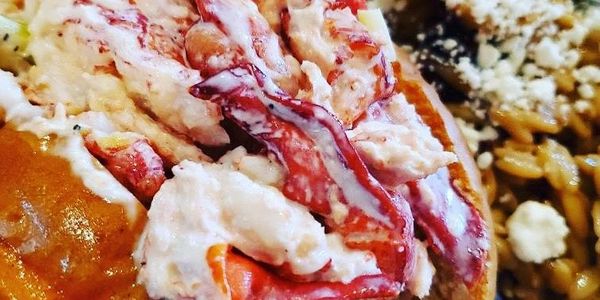 Close-up of lobster roll with creamy filling and a side dish.