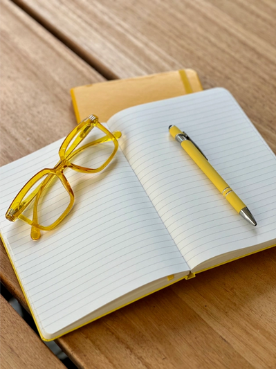 An open yellow marketing notebook with a pair of yellow glasses and a pen resting on top.
