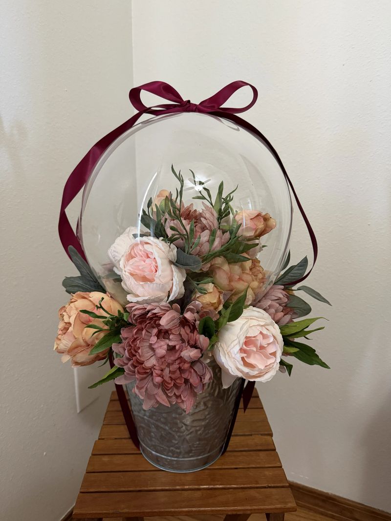 A balloon gift with silk flowers in a clear balloon with base.