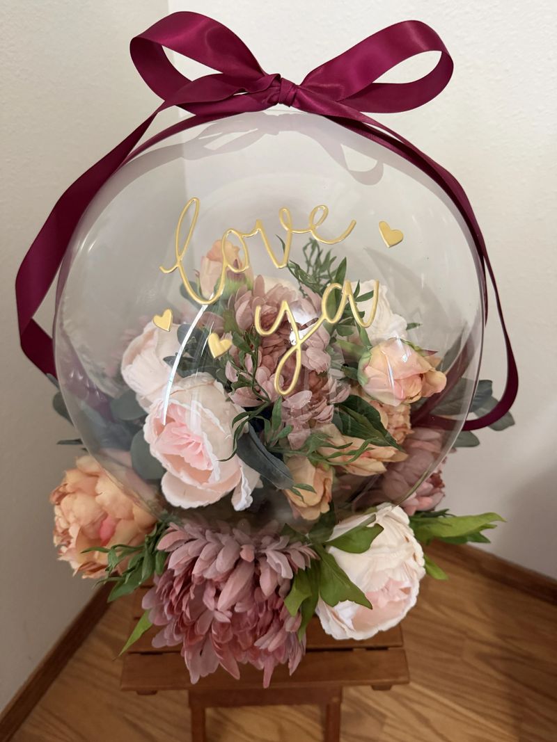 A balloon gift with silk flowers and Love Ya in a clear balloon with base.