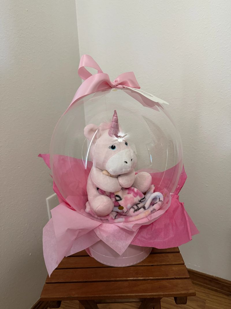 Baby Girl Balloon Gift with a soft toy unicorn in a clear ballon with basket base and bow.