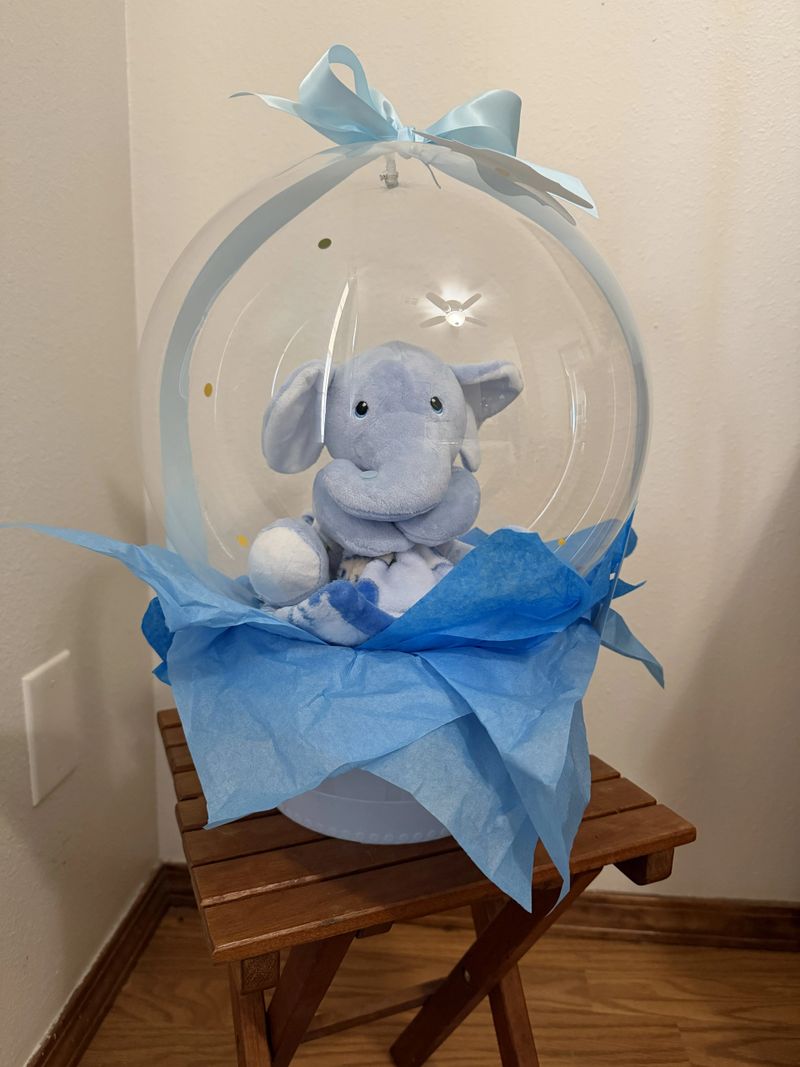 Baby Boy Balloon Gift with a soft toy elephant in a clear ballon with basket base and bow.
