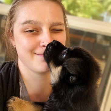 A woman smiling as a puppy licks her nose.