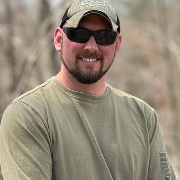 Smiling man wearing sunglasses and a cap outdoors.