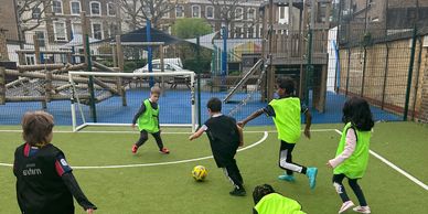 Children playing soccer on a small outdoor field with green jerseys.
