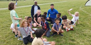 Children with medals and coaches celebrating on a soccer field.