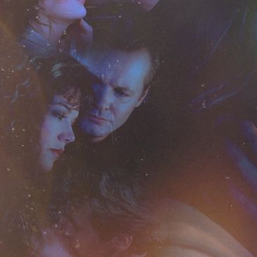 Two people lying close in an intimate setting with dim lighting.