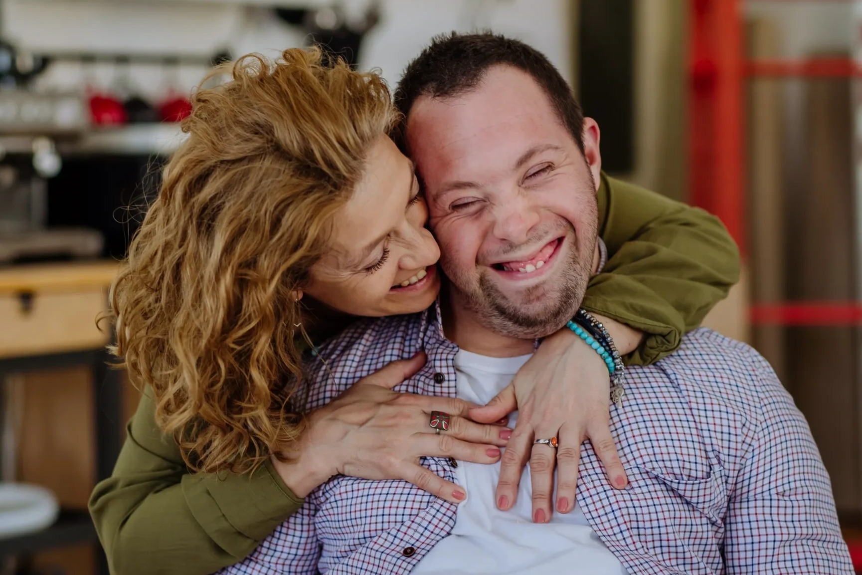 A woman affectionately hugging a man with Down syndrome, both smiling joyfully.