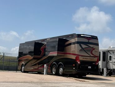 Luxury Prevost motorhome parked with slide-outs extended under a blue sky.