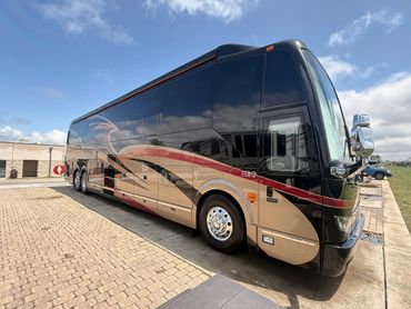 A luxury motorcoach with sleek black and beige design parked on a paved area.