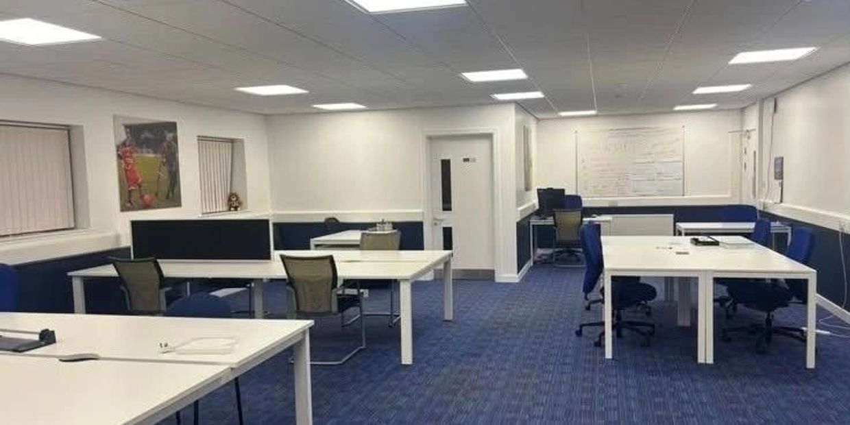 Modern office space with white desks and blue chairs on a blue carpet.