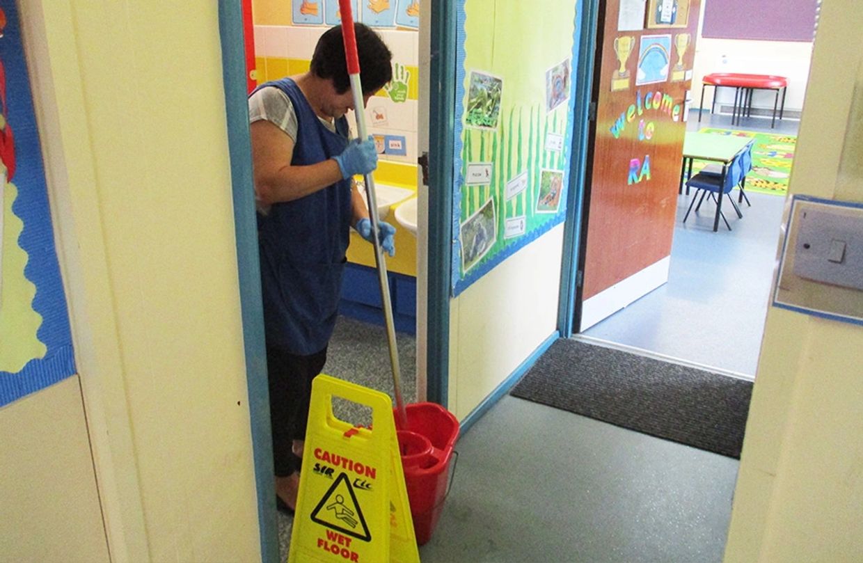 Janitor cleaning floor with mop and caution wet floor sign nearby.