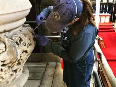 Person restoring ornate stonework indoors.