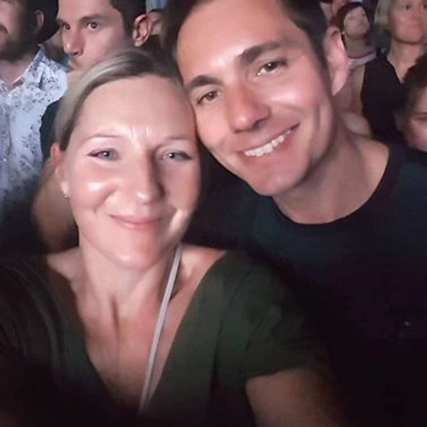 Two people smiling for a selfie at a crowded event.