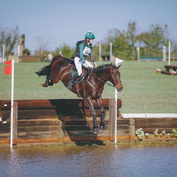 Equestrian rider jumps horse over water obstacle during competition.