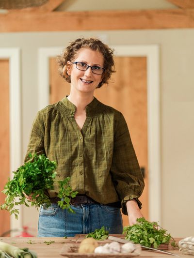 Smiling woman holding fresh herbs in a kitchen.