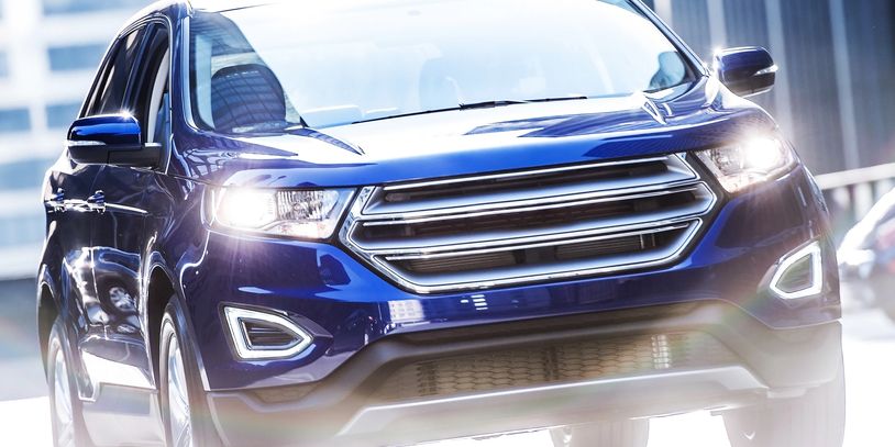 Blue SUV driving in a city with headlights on.