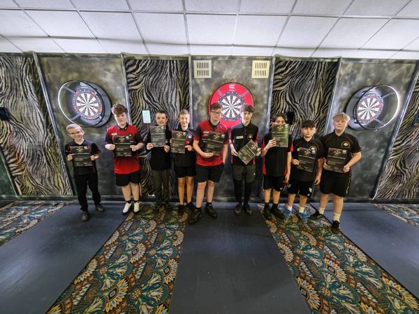 A group of nine boys holding certificates in front of dartboards.