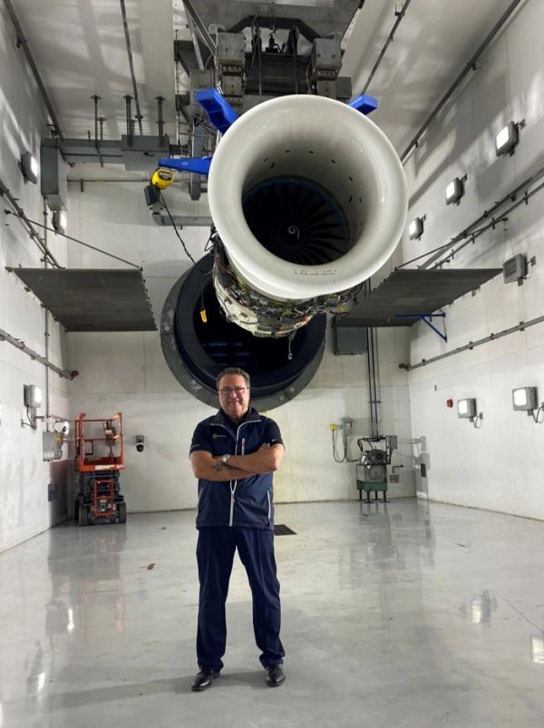 Man standing under an aircraft engine inside a hangar.