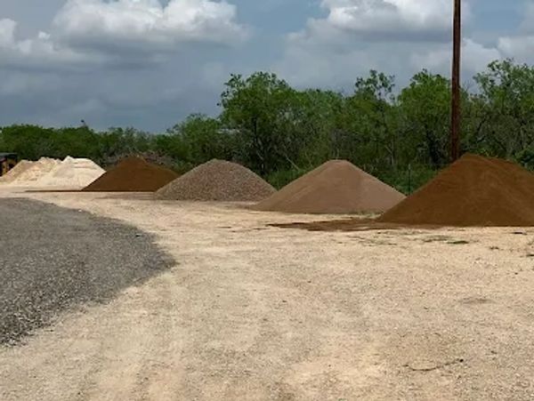Rows of different colored sand and gravel piles on a dirt road under a cloudy sky.