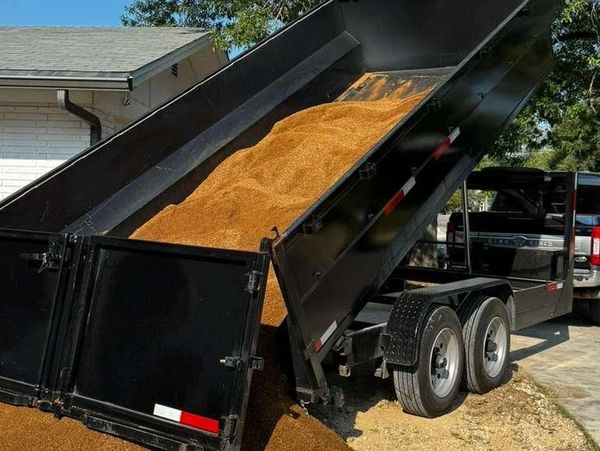 Black dump trailer unloading gravel or sand in a driveway.