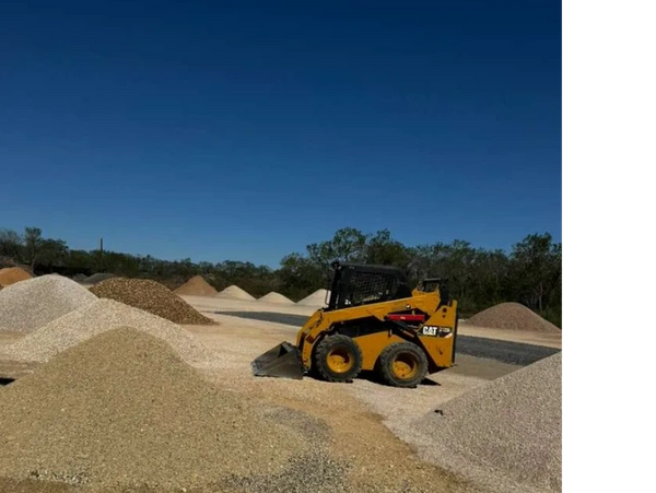 Yellow skid steer loader at a gravel yard with multiple gravel piles.