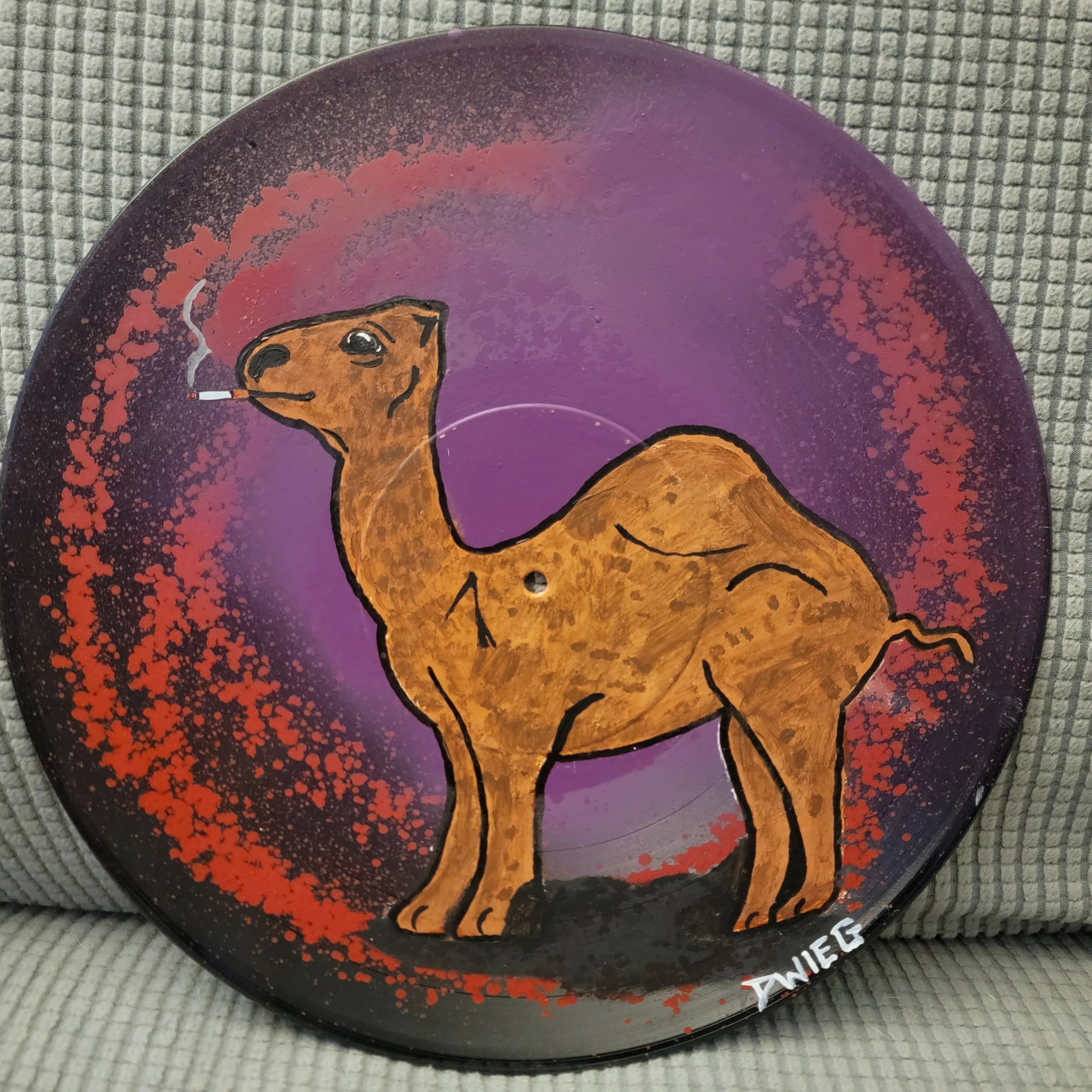 Painted camel smoking a cigarette on a purple and red-speckled disc.