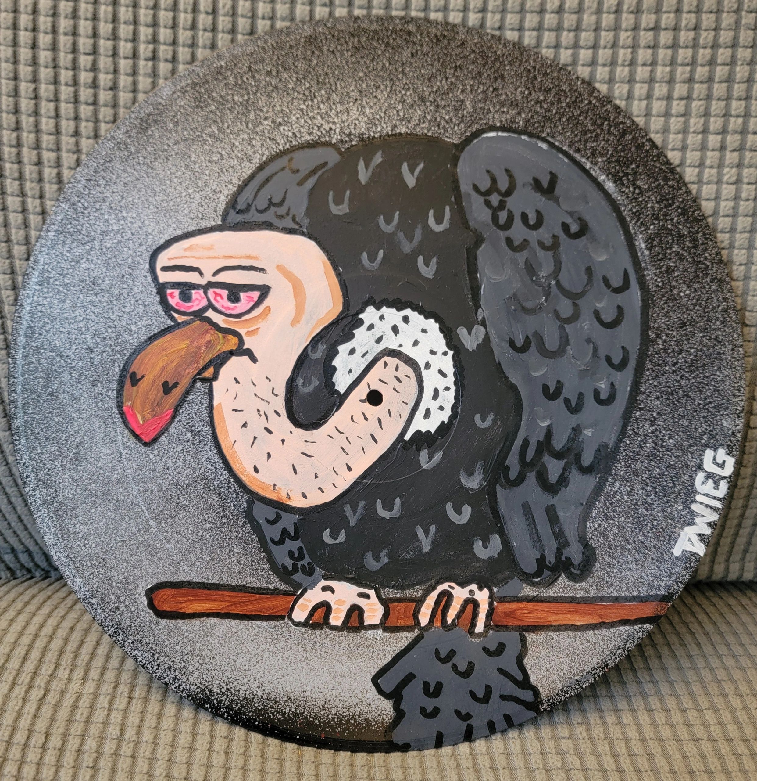 Cartoon vulture with red eyes perched on a branch, painted on a round textured surface.