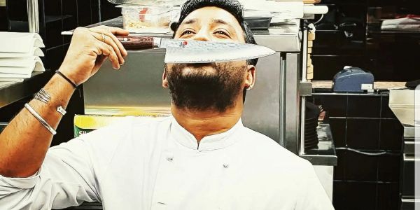 Chef holding a knife near his face in a kitchen.