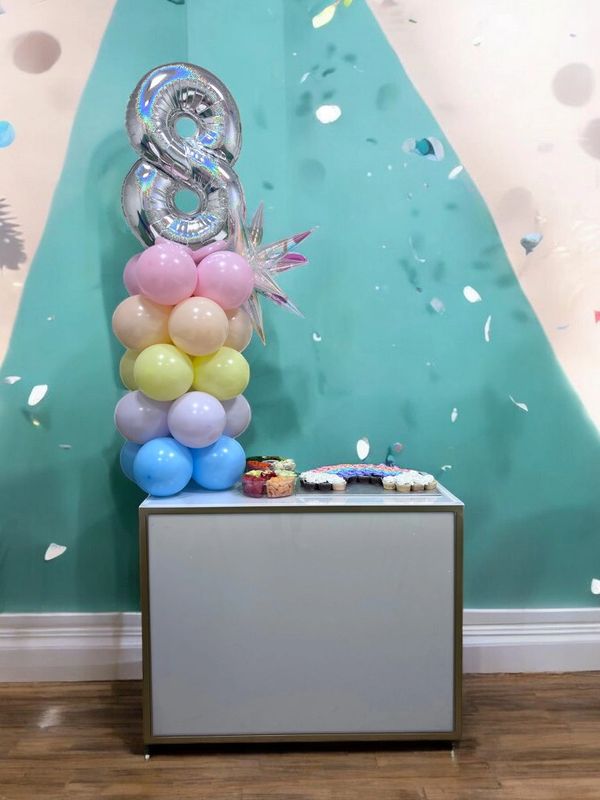 Colorful balloon tower with a silver '8' balloon on top beside a small table with snacks.