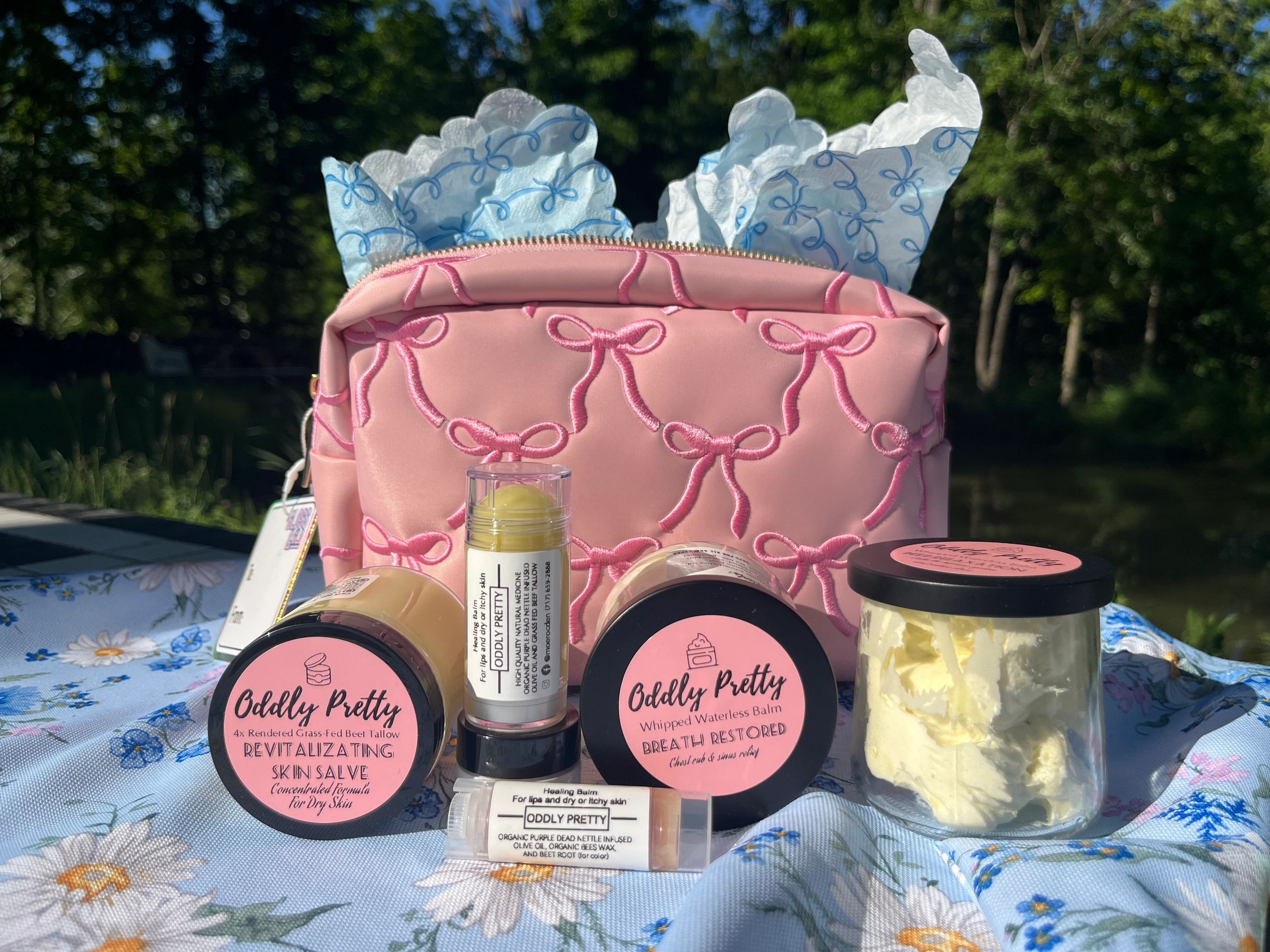 Beauty products displayed on a floral tablecloth with a pink bag in the background.