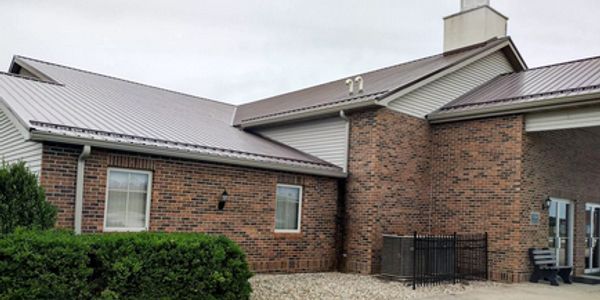 Brick and siding building with metal roof under cloudy sky.