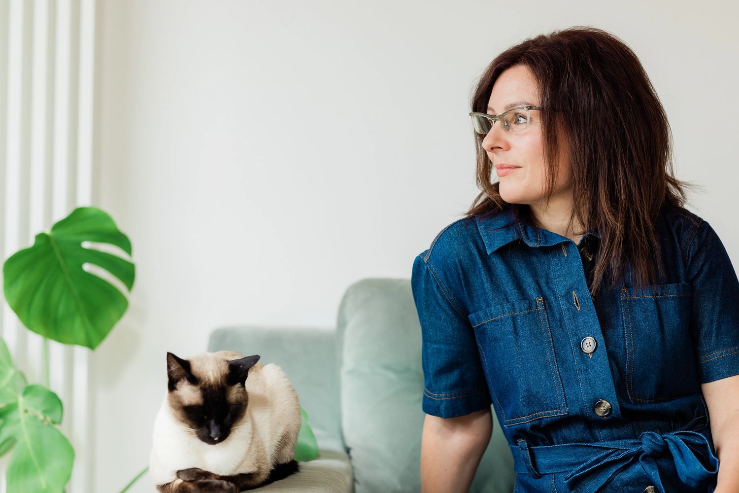 Kim from Style Your Home Happy with her  cat sitting on a sofa by a houseplant. Home Stager.