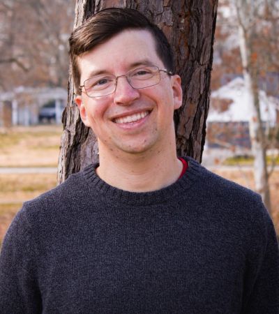 A man smiling in front of a tree outdoors.