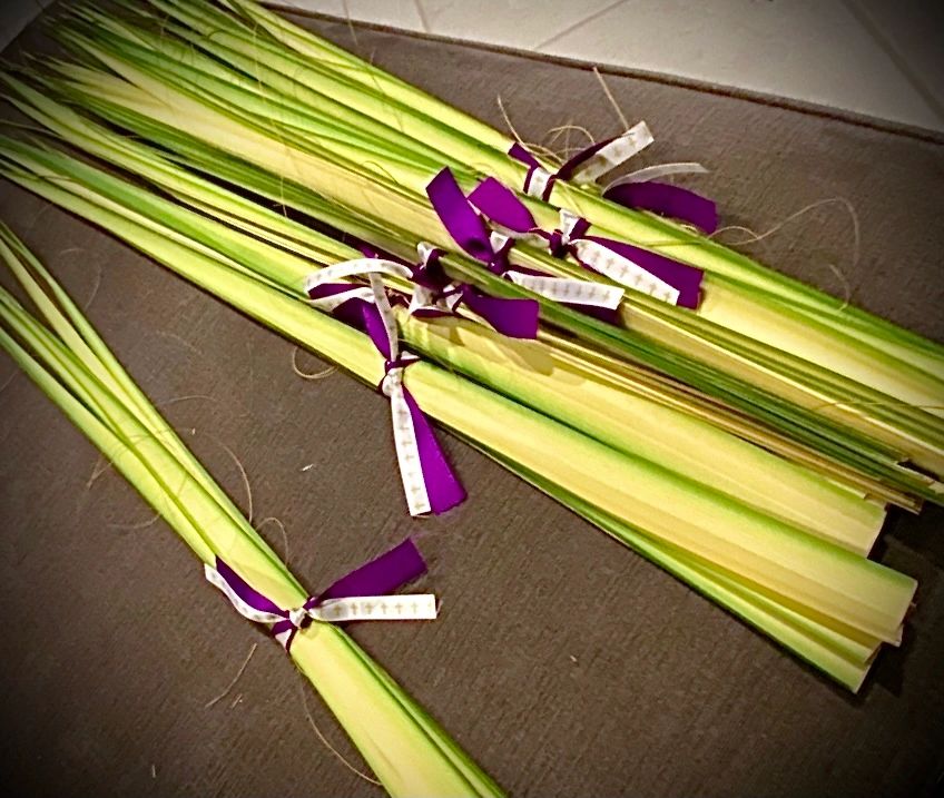 Bundles of palm leaves tied with purple and white ribbons.