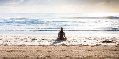 Person sitting in the shallow water on a beach looking out to sea
