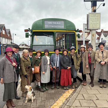 Group in vintage attire poses by a classic green bus on a street.