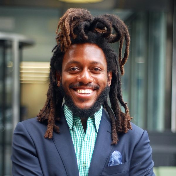 Smiling man with dreadlocks in a navy blazer.